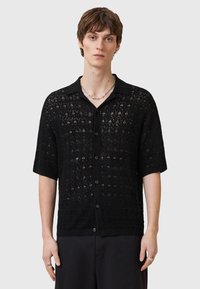 Camisa negra de manga corta con una textura similar a encaje, cierre frontal con botones y cuello. Patrón intrincado notable a lo largo de toda la tela.
