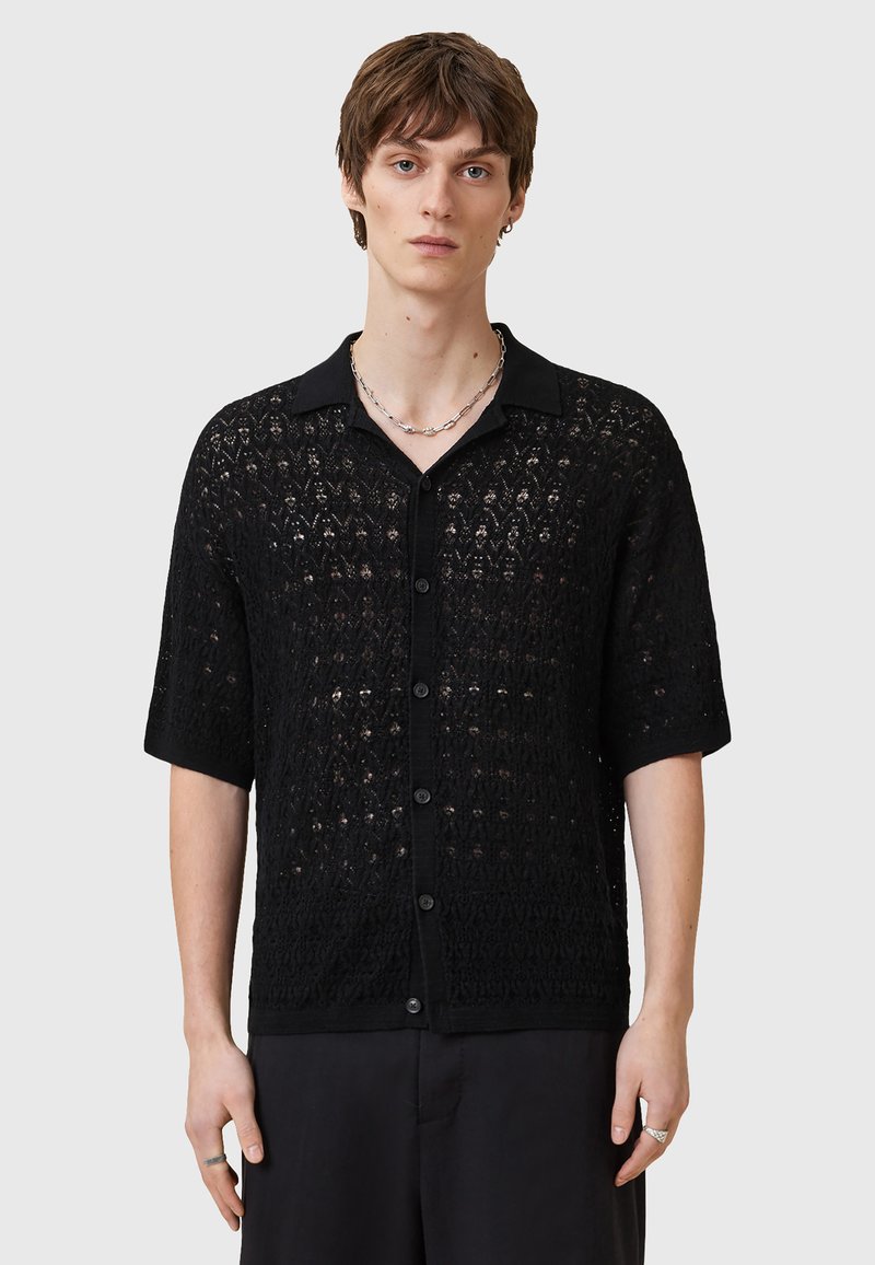 Camisa negra de manga corta con una textura similar a encaje, cierre frontal con botones y cuello. Patrón intrincado notable a lo largo de toda la tela.