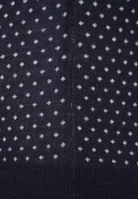 Mörkblå stickad tyg med vita prickar i ett enhetligt mönster, med en slät textur och synlig sömnad längs sömmarna.