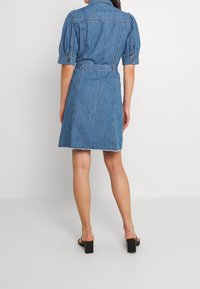 Denim-mekko, jossa on lyhyet puff-hihat, vyöllinen vyötärö ja risatoiset helmat. Ominaisuuksiin kuuluu vintagetyylinen muotoilu ja vaaleansininen väri.
