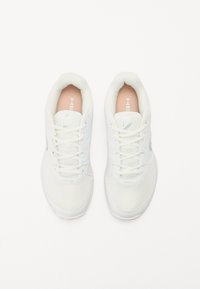 Weiße Sportschuhe aus Netz- und Synthetikmaterial, mit einer strukturierten Oberfläche, Schnürverschluss und dezentem Branding an der Seite und der Zunge.