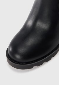 Mustat nahka ankle-bootit pyöreällä kärjellä, tekstuurilla varustetulla päällisellä ja paksulla, karkealla pohjalla. Saumatyöt reunojen ympärillä.