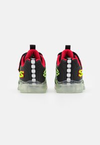 Black athletic shoes with red accents and neon green logo, featuring a textured upper, transparent sole, and a striped back design.