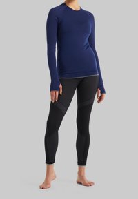 Námořnická modrá dlouhá sportovní tričko v kombinaci s černými legínami s texturovanými panely a přiléhavým střihem. Oba kousky jsou elastické a prodyšné.