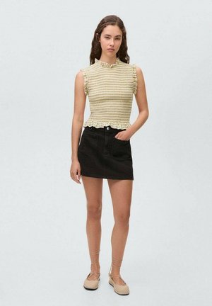 Gelbes Smock-Oberteil mit Rüschensäumen, kombiniert mit einem schwarzen Denim-Rock. Das Model trägt beige Espadrilles mit Schnürdetails.
