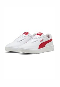 Baskets blanches avec une bande rouge de Puma, présentant une tige en cuir texturé, un bout rond, un design à lacets et un col rembourré.