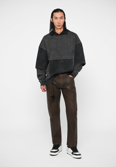 Hooded majica u tamnosivoj boji s teksturiranim uzorcima, oversized rukavima i logotipom. Uparen s smeškastim hlačama i crno-belim patikama.