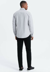 Vaaleanharmaa nappikauluspaita pitkillä hihoilla, mustat housut ja mustat lenkkarit. Paidassa on perinteinen kaulus ja yksinkertainen muotoilu.