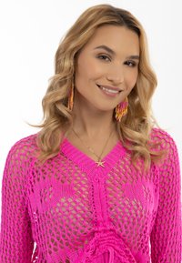 Helles pinkes Strickpullover mit einem Rautenmuster. Verfügt über einen tiefen V-Ausschnitt, strukturierte Details und einen Lagenlook.