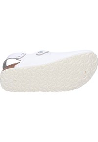 White slip-on shoe with a curved design, featuring a grey strap and textured rubber sole. The sole has a patterned tread for grip.