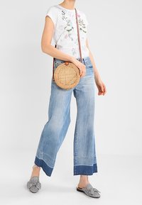 Bílá tričko s květinovým potiskem, světle modré široké džíny, tkaná kruhová přes rameno taška a kostkované slip-on boty.