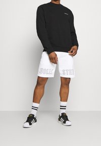 Svart sweatshirt, vita shorts med "HOLLISTER" tryckt, svart och vita sneakers och randiga strumpor. Enkel, modern sportklädsel.