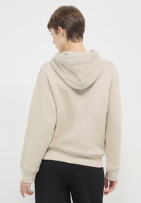 Felpa con cappuccio beige dal fit rilassato, con polsini e orlo a coste. Tessuto morbido; design minimalista; presenta un cappuccio grande e morbido.