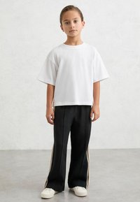 T-shirt blanc à manches courtes de coupe ample accompagné d'un pantalon de survêtement noir avec des bandes latérales et des baskets blanches. Design simple et décontracté.