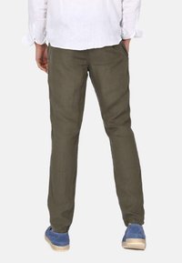 Olivově zelené lněné kalhoty se střihem rovné nohavice, vybavené bočními kapsami. Na nohou modré plátěné espadrilky. Zobrazena zadní část.