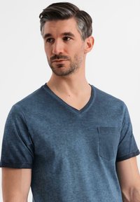 Námořnická modrá V-krční tričko vyrobené z měkké látky, s krátkými rukávy a malou náprsní kapsou s jemnou texturou.