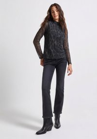 Zwarte lange mouwen top van mesh met luipaardpatroon, gecombineerd met donkere jeans met rechte pijpen en zwarte enkellaarzen. Eenvoudige, aansluitende silhouet.