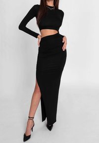 Musta pitkähihaine crop-top, joka on yhdistetty tiukkaan mustaan maxi-hameeseen, jossa on korkea sivuleikkaus ja ryppyinen rakenne. Korkeat korkokengät viimeistelevät ilmeen.