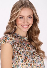 Bluză cu un model floral, având mâneci volanate, cu forme geometrice multicolore în nuanțe de portocaliu, verde și roz, pe un fundal deschis.