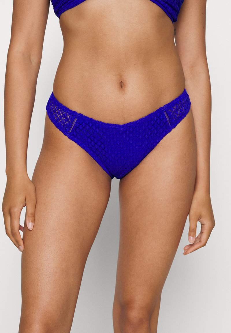 Tangas de biquíni azuis, tricotadas, com um padrão texturizado, um corte baixo e laterais largas para maior conforto. O tecido parece ser elástico e respirável.