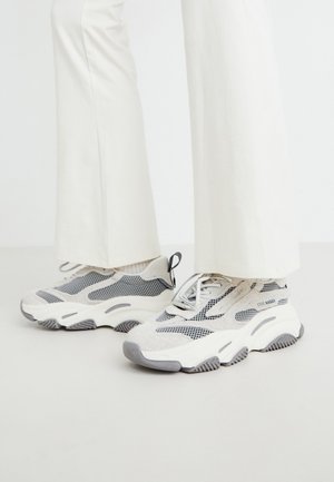 Grosse atletske teniske v svetlo sivi barvi, ki združujejo mrežaste in tekstilne materiale, s patterned elementi in debelim gumijastim podplatom.