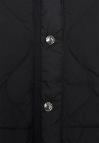 Svart kviltad jacka med en slät textur, med silverfärgade tryckknappar och en vertikal knappslå.