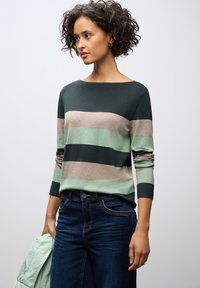 Gestreifter Pullover in dunkelgrün, weichem Mint und Beige. Mit Bootsausschnitt, langen Ärmeln und gerippten Bündchen. Kombiniert mit dunklen Jeans.