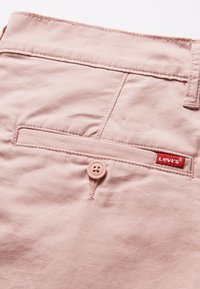 Pantalon en coton rose clair avec une poche arrière bordée de surpiqûres et une petite étiquette rouge Levi's, complété par un bouton assorti.