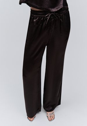 Black satin wide-leg pants with drawstring waist worn with silver strappy open-toe heels on a neutral background.