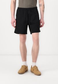 Sorte shorts med elastisk talje og snøre, der har en glat tekstur og en afslappet pasform. Bæres med beige sneakers og hvide sokker.