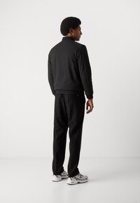 Jachetă neagră căptușită cu guler înalt, manșete elastice și pantaloni negri asortați. Purtați cu pantofi sport gri și albi.