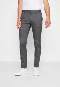 Šedé slim-fit kalhoty vyrobené z lehké látky. Mají standardní pas, přední kapsy a hladkou strukturu. Nošeny s bílými teniskami.