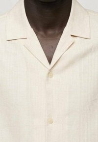Beiges Leinen-Kurzarmhemd mit Schlitzkragen, besitzt eine feine Struktur und zwei Knöpfe vorne.