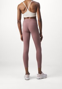 Leggings de sport en mauve, taille haute, en tissu extensible, associés à un soutien-gorge de sport clair et à des chaussures de sport blanches.