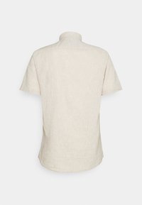 Chemise beige à manches courtes en tissu texturé, vue de dos avec un col montant et un ourlet légèrement arrondi.