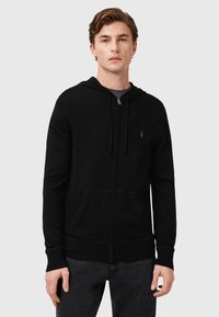 Sudadera con cremallera negra hecha de un tejido suave, que cuenta con un bolsillo tipo canguro, capucha ajustable con cordón y un pequeño logo en el pecho.