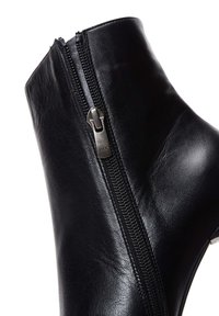 Bottine en cuir noir avec fermeture éclair sur le côté et forme élégante. La surface a une texture lisse avec un éclat subtil et un matériel minimal.