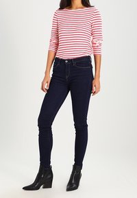 Maglietta a maniche lunghe a righe rosse e bianche con scollatura ampia, abbinata a jeans skinny blu scuro e stivaletti neri alla caviglia con tacco largo.