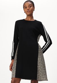 Schwarzes Kleid mit langen Ärmeln und weißen Streifen. Seitenteil aus Leoplarddruckstoff. Runder Halsausschnitt und lockerer Schnitt.