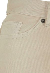 Béžová denimová tkanina s texturovaným vzorem, obsahující přední kapsu a kovové knoflíky s nápisem "Urban Classics."