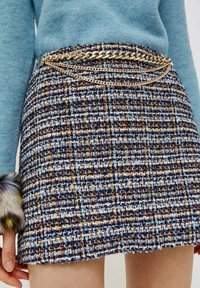 Spódnica z tkanego tweedu w kratkę w odcieniach niebieskiego, białego i wielokolorowych nici, z metalicznym łańcuszkiem w pasie.