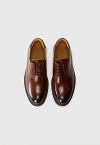 Pantofi de dress din piele maro cu o finisare netedă, vârf rotund și sistem de închidere cu cinci găuri pentru șireturi. Dispune de un limba căptușită și o branț confortabil.