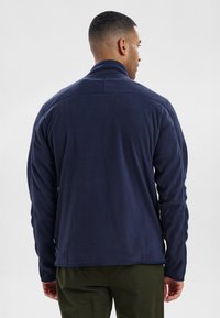 Chaqueta de forro polar navy con un cuello alto, mangas largas y una superficie texturizada. La parte posterior presenta una costura a lo largo de los hombros.