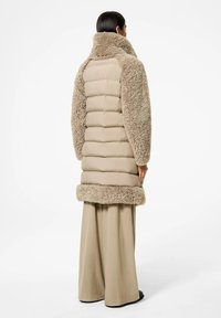 Cappotto imbottito beige con dettagli in pelliccia, caratterizzato da un colletto alto, design a trapunte orizzontali e un bordo in pelliccia morbida e testurizzata all'orlo e alle maniche.