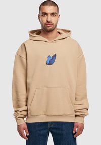 Beige hoodie med stor frontlomme, lavet af bomuldsstof, med et blåt sommerfuglegrafik i midten, afslappet pasform og snoretræk i hætten.