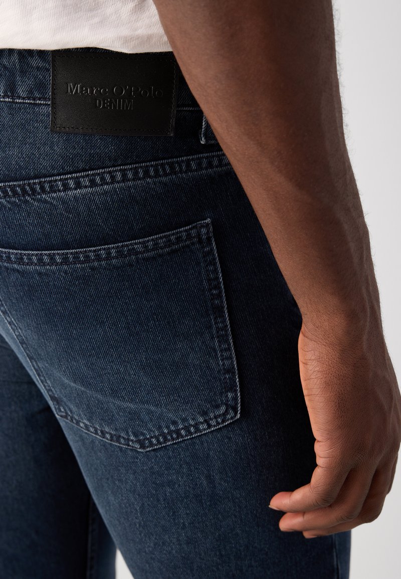 Ciemnoniebieskie dżinsy wykonane z denimu, z tylną kieszenią, skórzaną naszywką z logo "Marc O'Polo DENIM" oraz gładkim, teksturowanym wykończeniem.