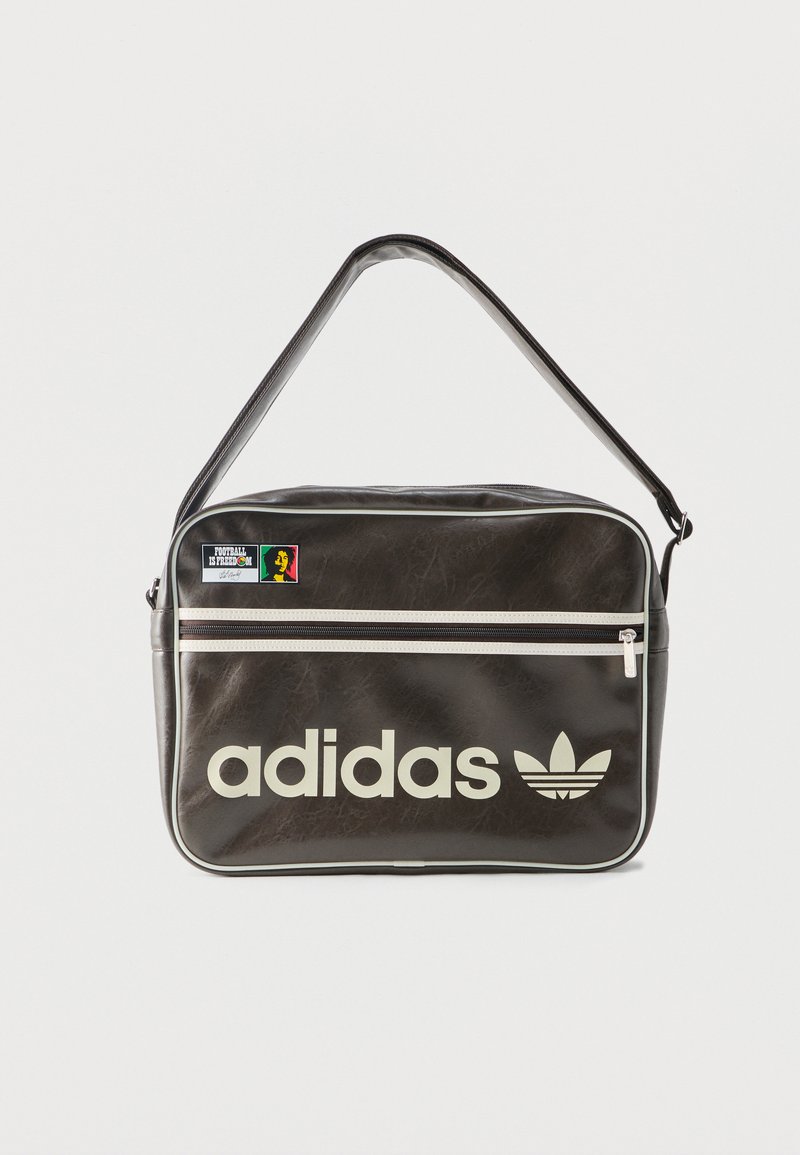 Borsa a tracolla Adidas nera con cerniera bianca, logo e toppa "Il calcio è libertà" sulla tasca anteriore.