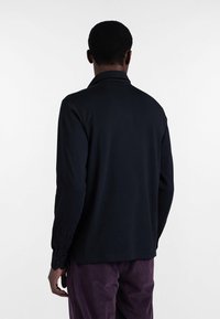 Schwarzes Langarmhemd mit Kragen, ausgestattet mit geknöpften Manschetten und geradem Saum. Glatte Textur, einfaches Design ohne Muster.