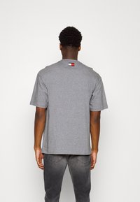 Harmaa puuvillapaita lyhyillä hihoilla, jossa on pieni logo-osa punaisella, sinisellä ja valkoisella yläselässä. Rento malli.