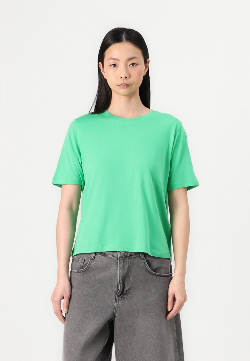 T-shirt vert à manches courtes en coton lisse avec un col rond, porté avec un pantalon en denim gris taille haute. Design simple, coupe lâche.